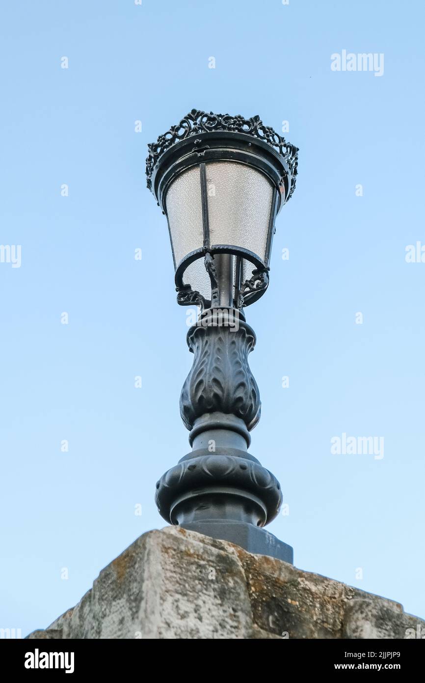 Un'inquadratura verticale, ad angolo basso, di una luce stradale ornamentale nera isolata su uno sfondo di cielo blu Foto Stock