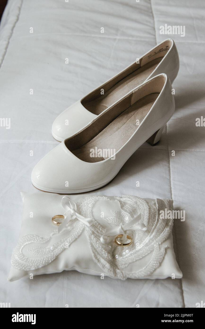 closeup verticale di scarpe da matrimonio bianche e anelli d'oro in attesa del loro proprietario Foto Stock