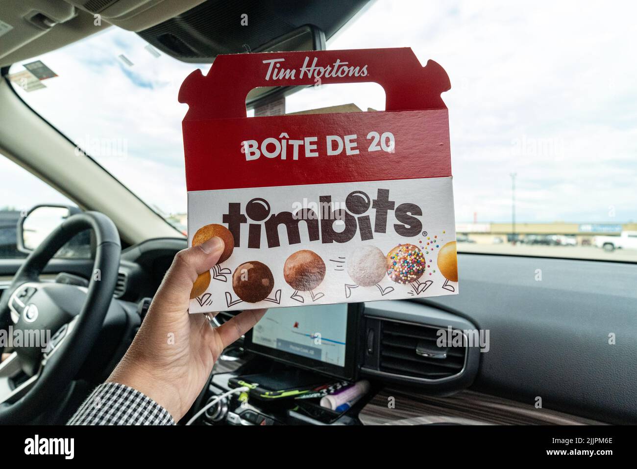 Pincher Creek, Alberta, Canada - 6 luglio 2022: Mano tiene in mano una scatola di Tim Horton's Timbits buchi di ciambella, mentre in auto Foto Stock