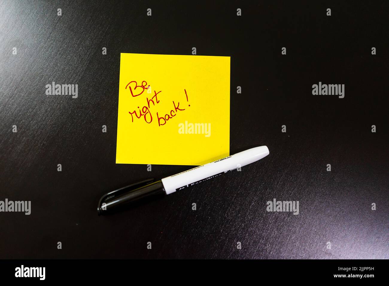 Un testo "Be Right BACK" scritto in un post-it giallo con la penna su una tabella Foto Stock