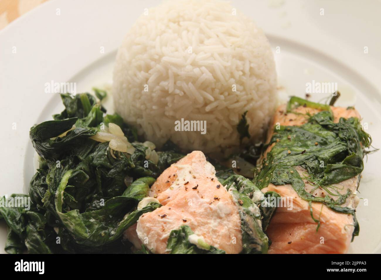 Un primo piano di cibo sano in un piatto con riso, pesce e alcuni verdi Foto Stock