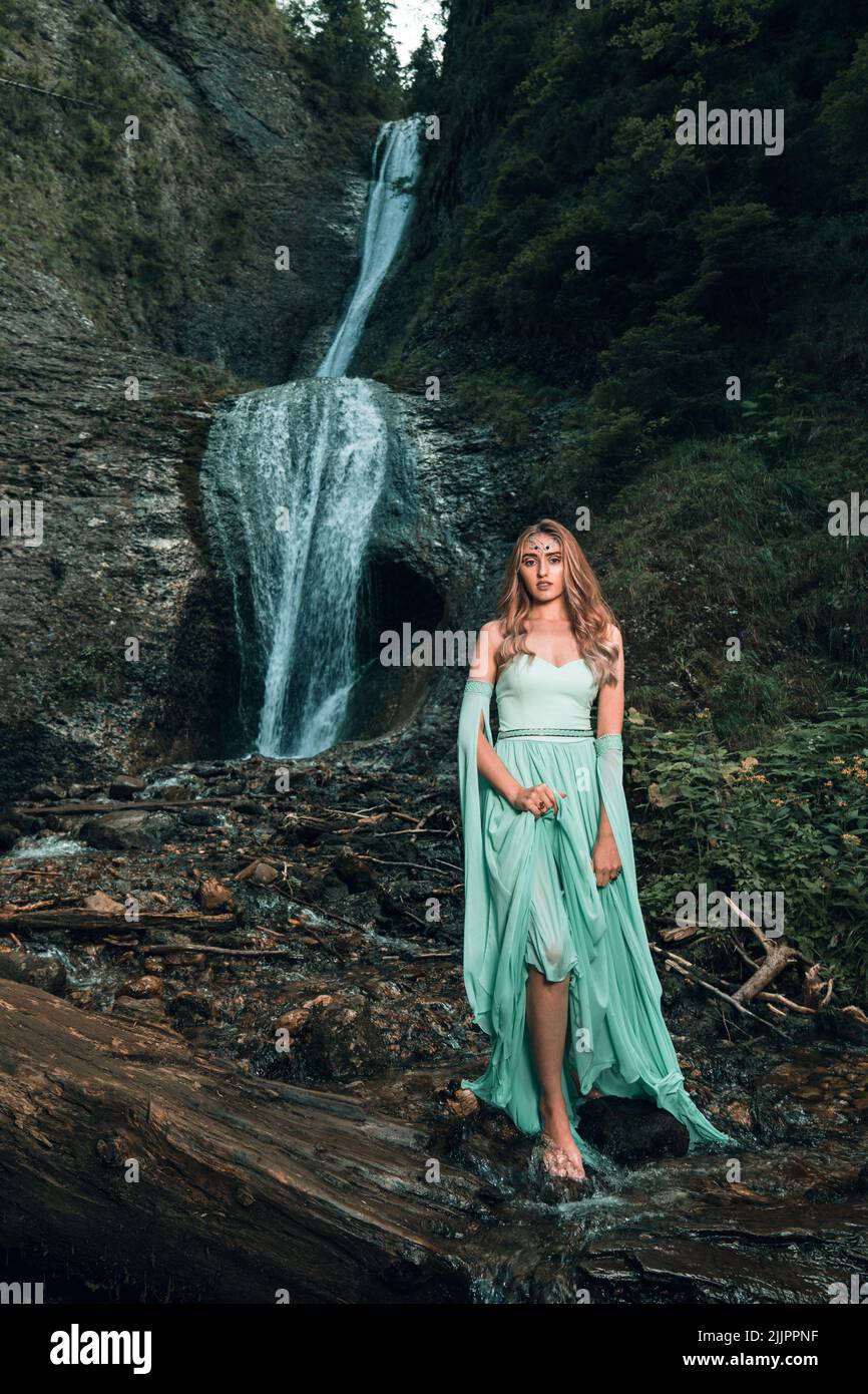 Una bella vista di una giovane donna con abiti tradizionali rumeni in piedi vicino a una cascata Foto Stock