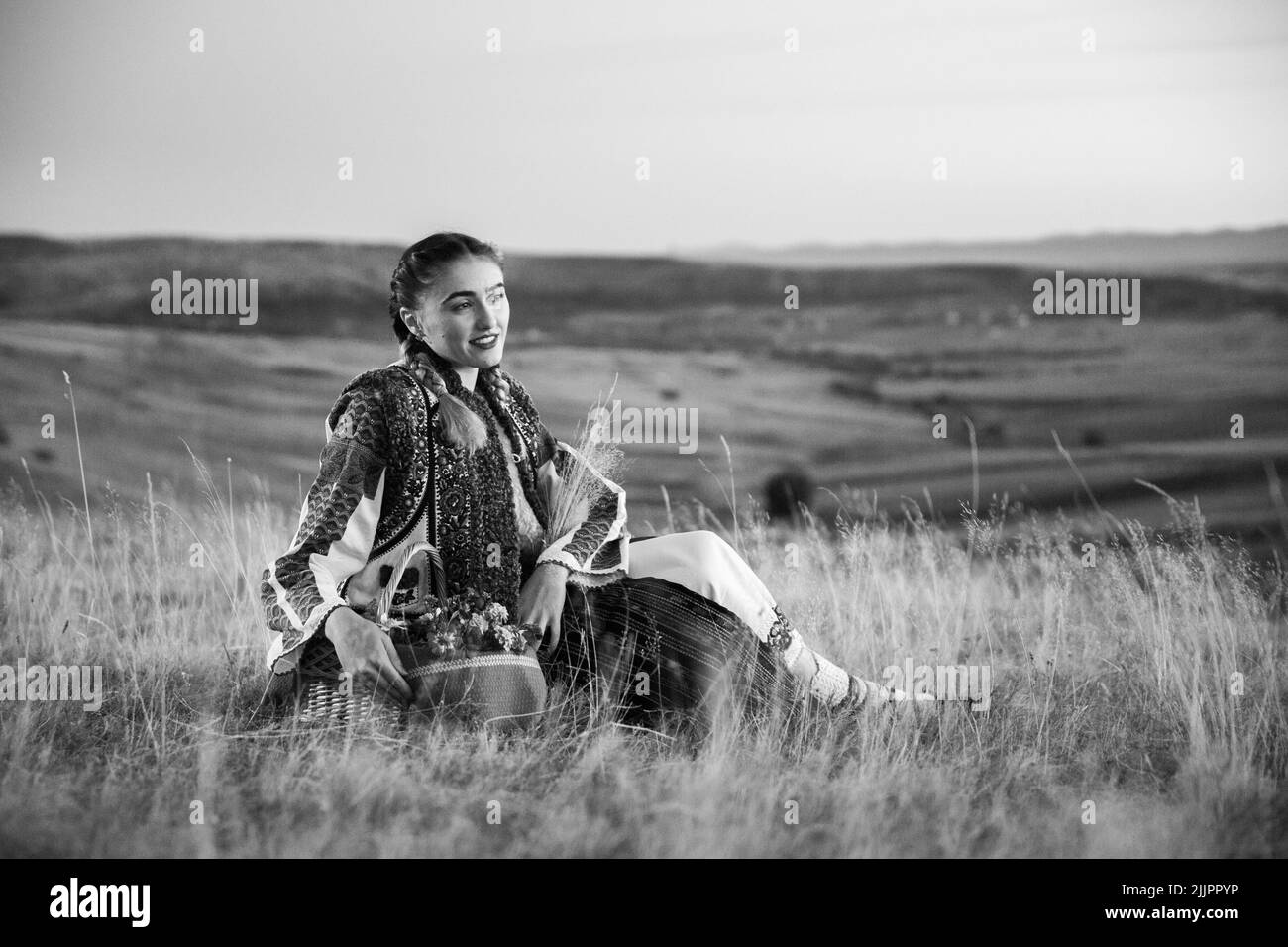 Una giovane donna rumena in costume tradizionale e cesto in posa sul campo Foto Stock