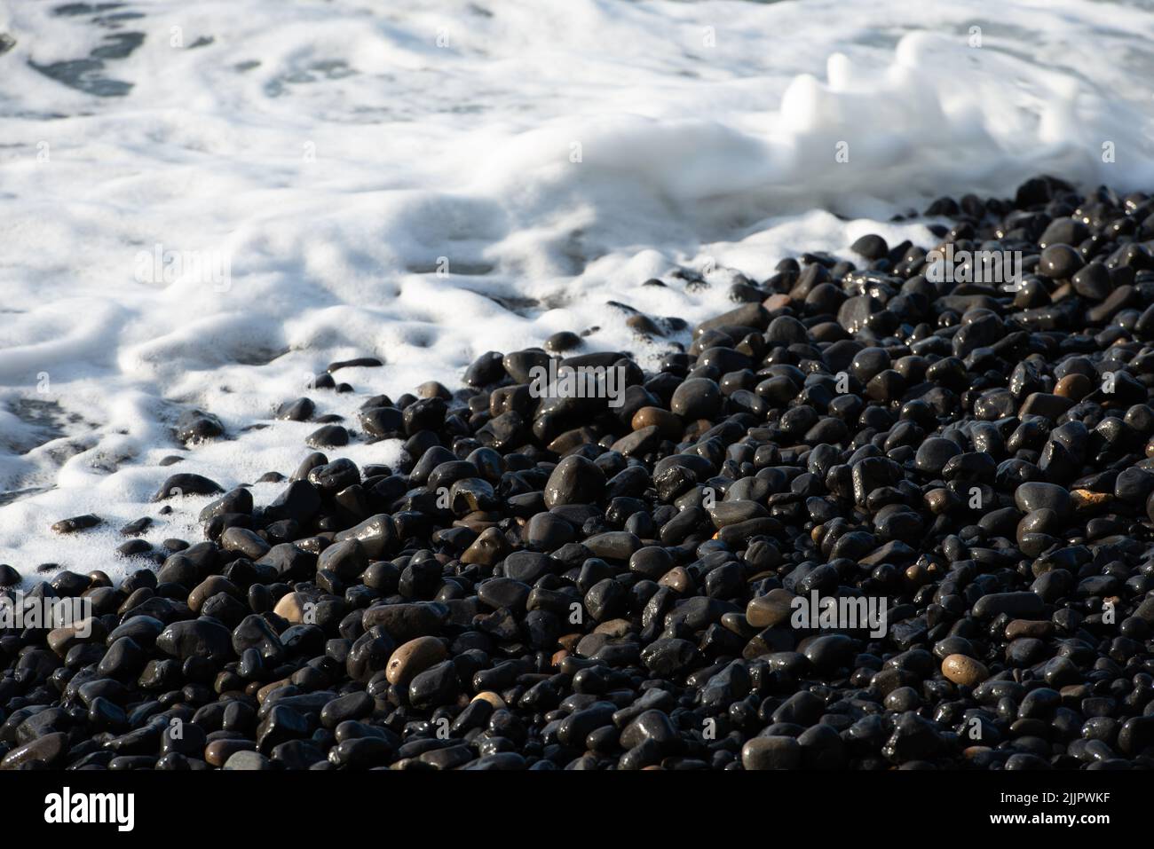 Onde che si infrangono sui ciottoli vulcanici neri della spiaggia di Mavra volta sull'isola di Chios in Grecia. Foto Stock