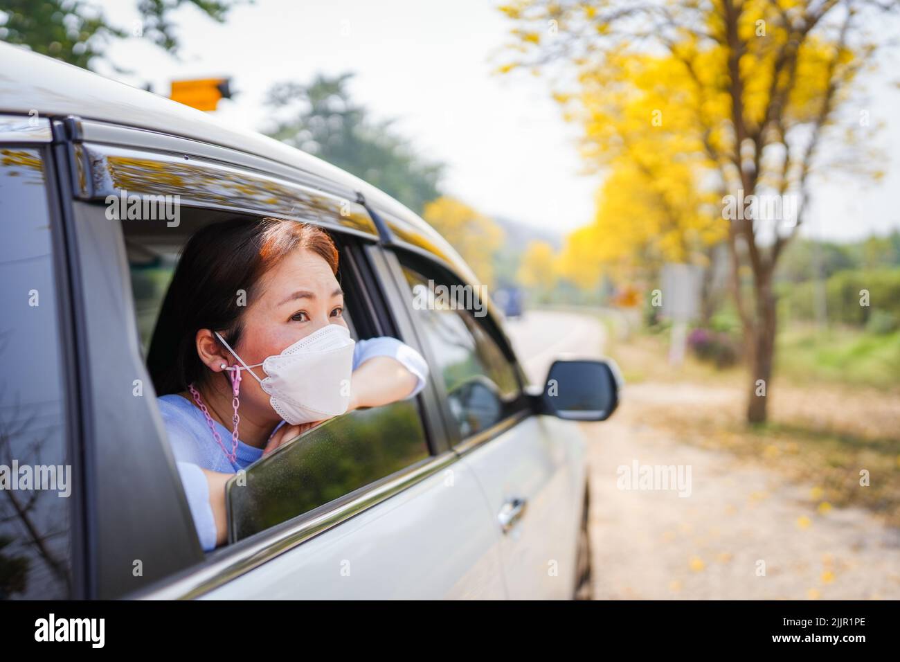 Una bella donna del sud-est asiatico in una maschera che guarda fuori dalla finestra dell'auto Foto Stock