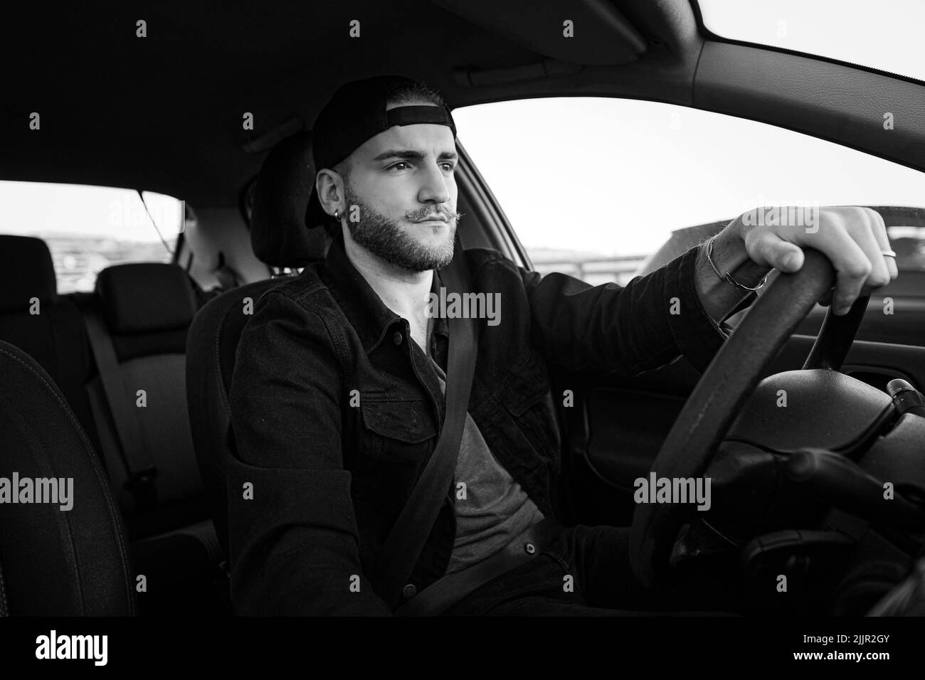 Un'immagine in scala di grigi di un bell'uomo caucasico che guida un'auto che indossa una cintura di sicurezza Foto Stock