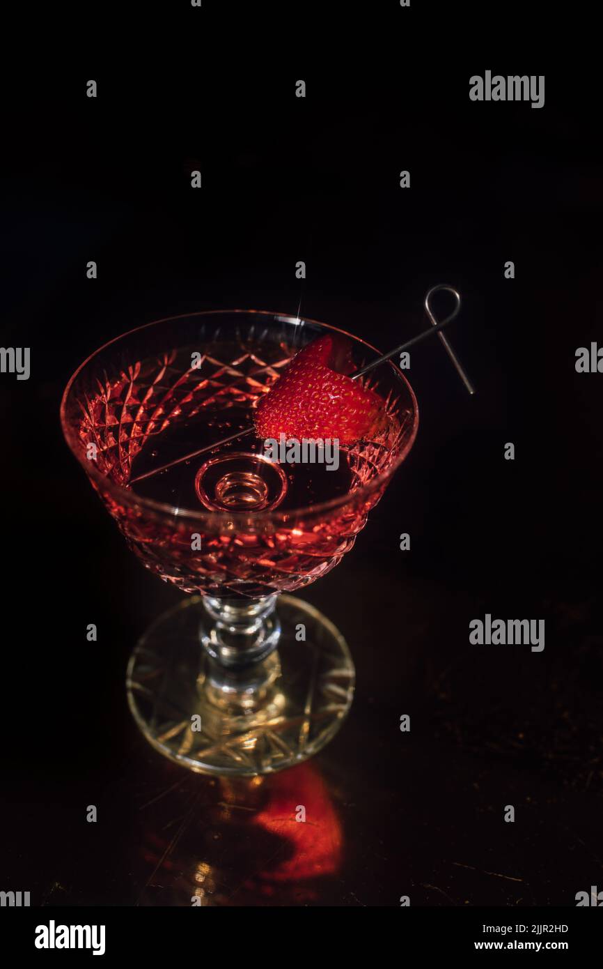 Un colpo verticale di un cocktail alcolico in un bel bicchiere con una fragola sulla paglia Foto Stock
