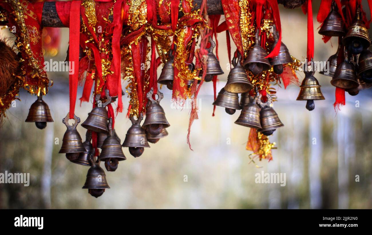 Una collezione di piccole campane in ottone su un nastro rosso appeso nell'aria Foto Stock