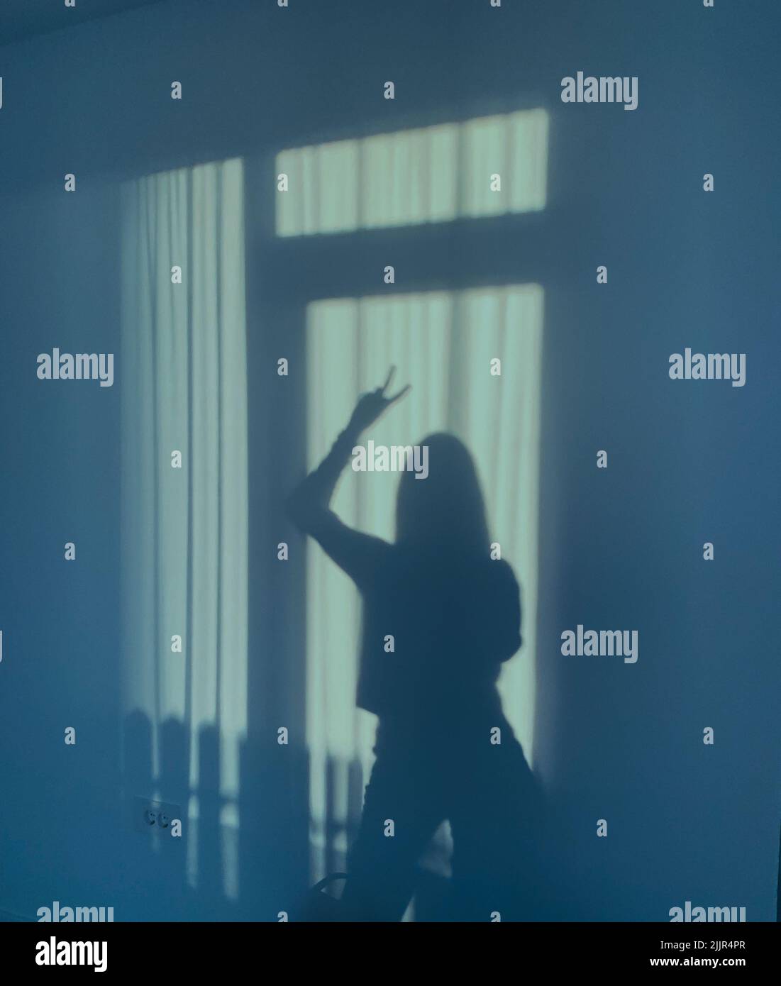 Una silhouette di una donna sul muro in piedi accanto alla finestra e la sua mano in su facendo un segno di V. Foto Stock