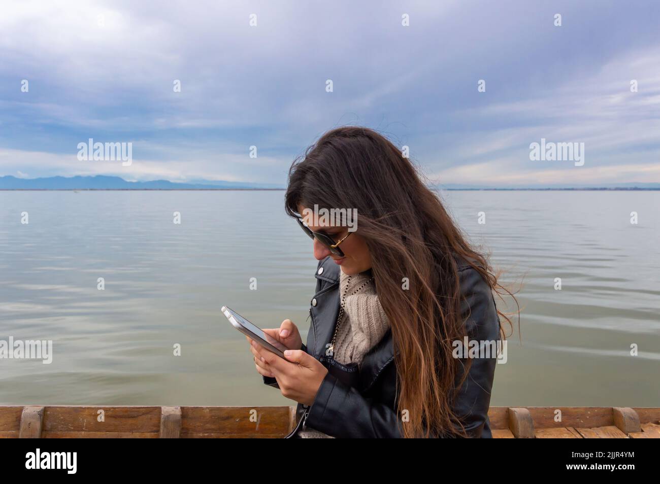 Una bella foto di una donna caucasica in piedi con il suo telefono di fronte a un mare Foto Stock