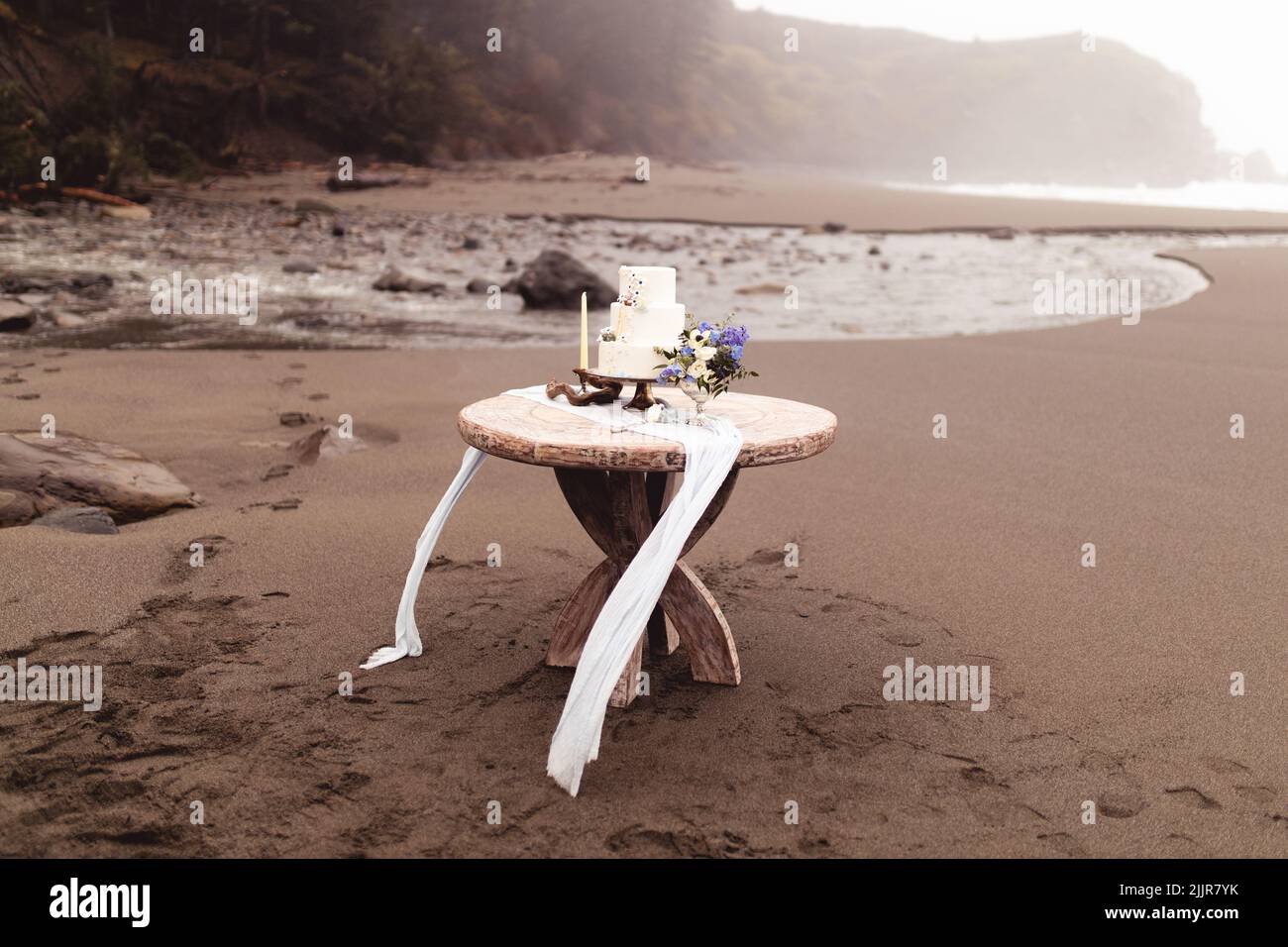 La torta nuziale con fiori e decorazioni su un tavolo di legno su una spiaggia di sabbia Foto Stock