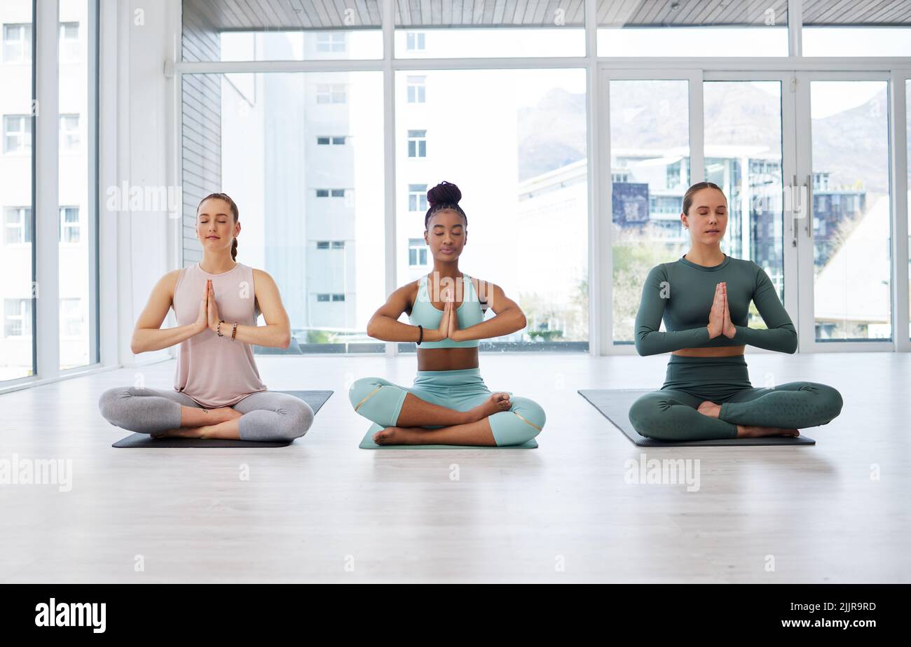 Inizia la tua giornata con la giusta atmosfera. Scatto completo di un gruppo di donne diverse sedute insieme in uno studio di yoga e meditating. Foto Stock