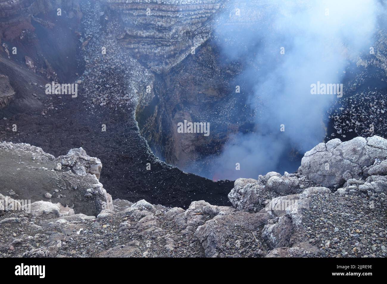 Un colpo ad angolo alto delle pietre ad un vulcano attivo con fumo. Foto Stock