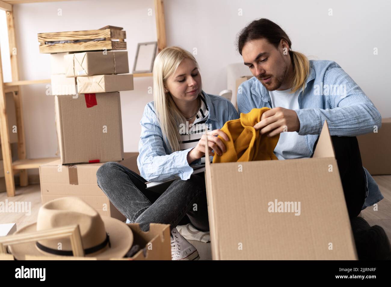 Un uomo e una donna nel giorno del movimento si siedono sul pavimento e si disimballano le cose. Felice coppia in un nuovo appartamento. Il concetto di affittare e comprare una casa Foto Stock