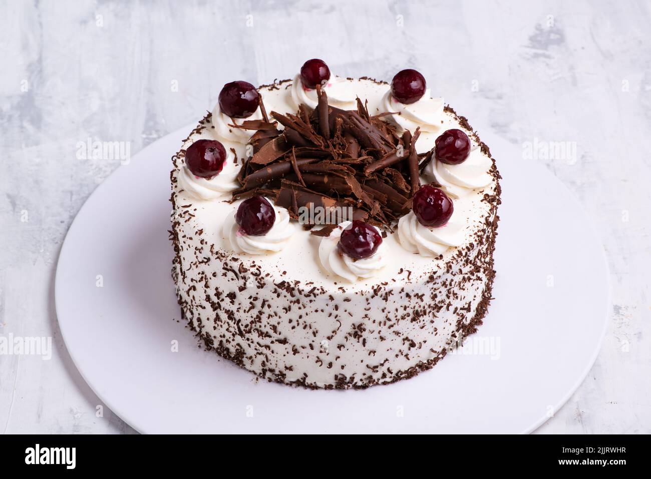 Un primo piano di crema bianca su torta di altopiano della Foresta Nera con ciliegie sulla superficie di marmo bianco Foto Stock