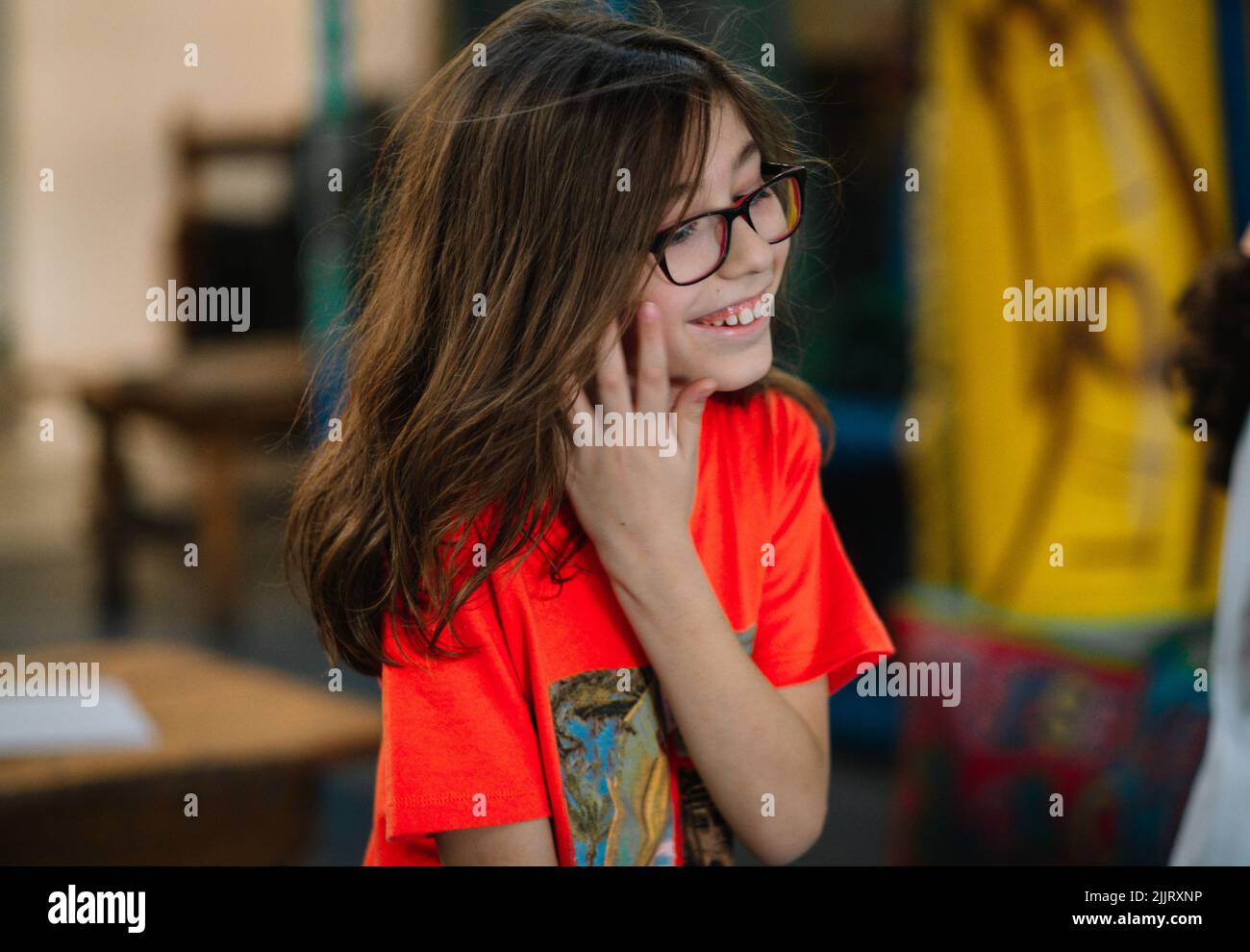 Un primo piano di un ragazzo caucasico con lunghi capelli brunette e bicchieri sorridenti e posati Foto Stock