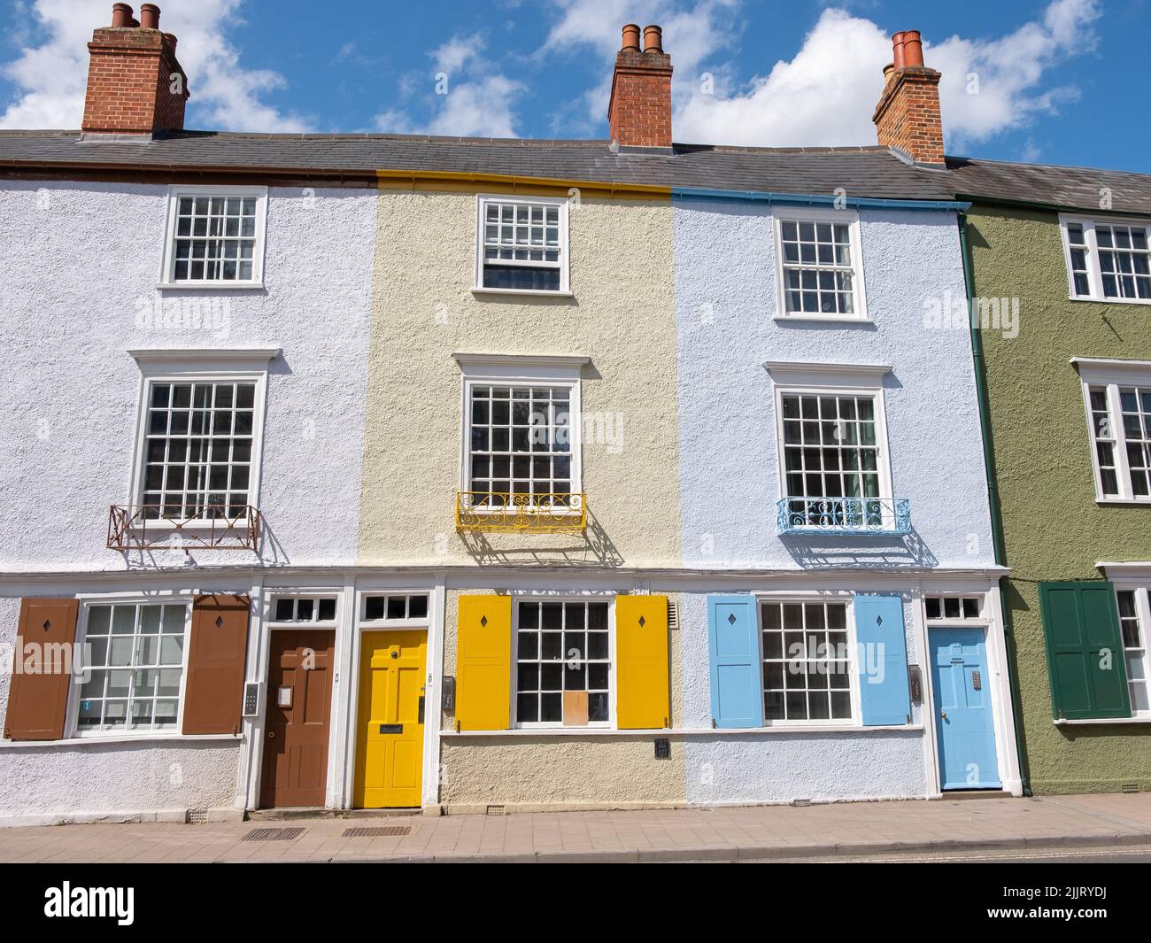 Tre case in mattoni stucco sono attaccate con camino e porte di colore marrone, giallo e blu lungo una strada a Oxford in una luminosa giornata di sole. Foto Stock