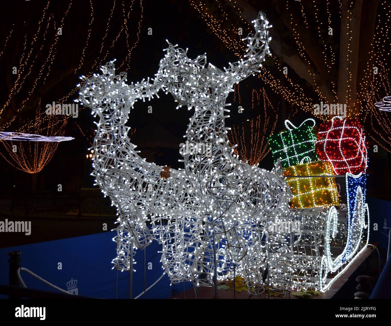 Un primo piano di renne con una slitta piena di regali decorati con luci di Natale Foto Stock