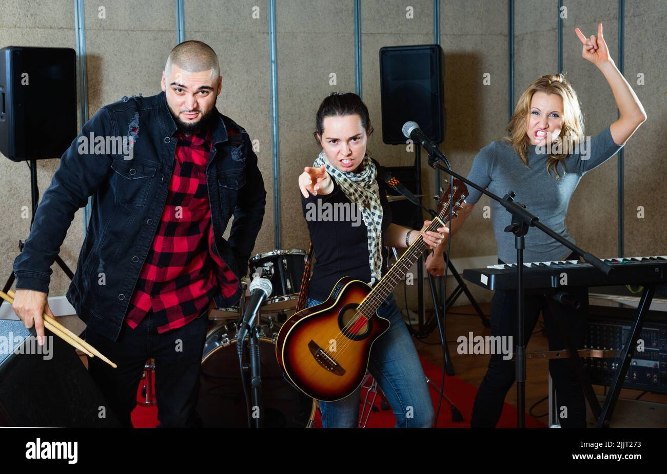 Tre bandmates che si posano insieme a strumenti musicali nella sala delle prove Foto Stock
