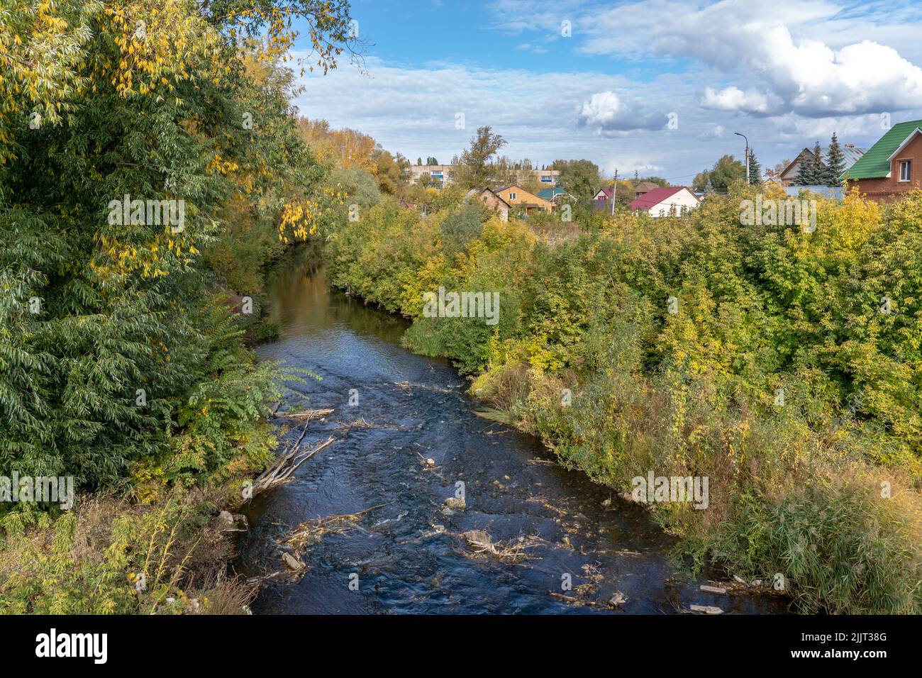 Paesaggio autunnale. Fiume all'interno della città di Sterlitamak, Repubblica di Bashkortostan. Il fogliame dorato cresce sulla riva, sotto il cielo blu con le nuvole Foto Stock