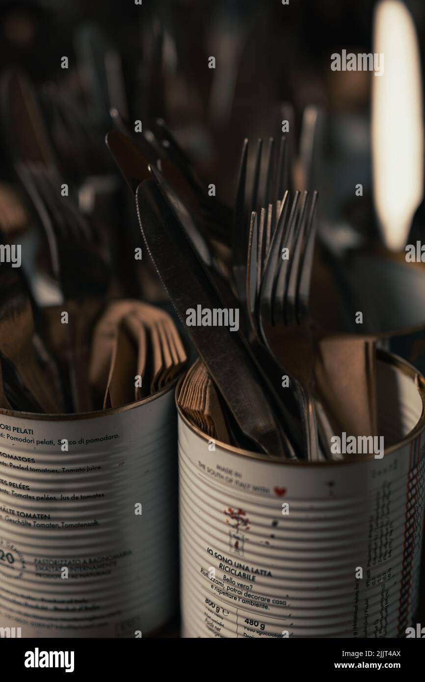 Un colpo verticale di posate, forchette, coltelli in lattine metalliche nella sala da pranzo del villaggio Foto Stock