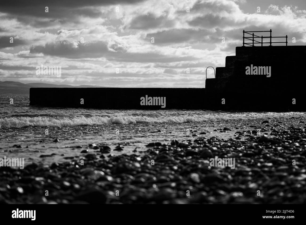 Un mare bianco e nero, spiaggia selvaggia, onde che colpiscono il muro di pietra del molo Foto Stock
