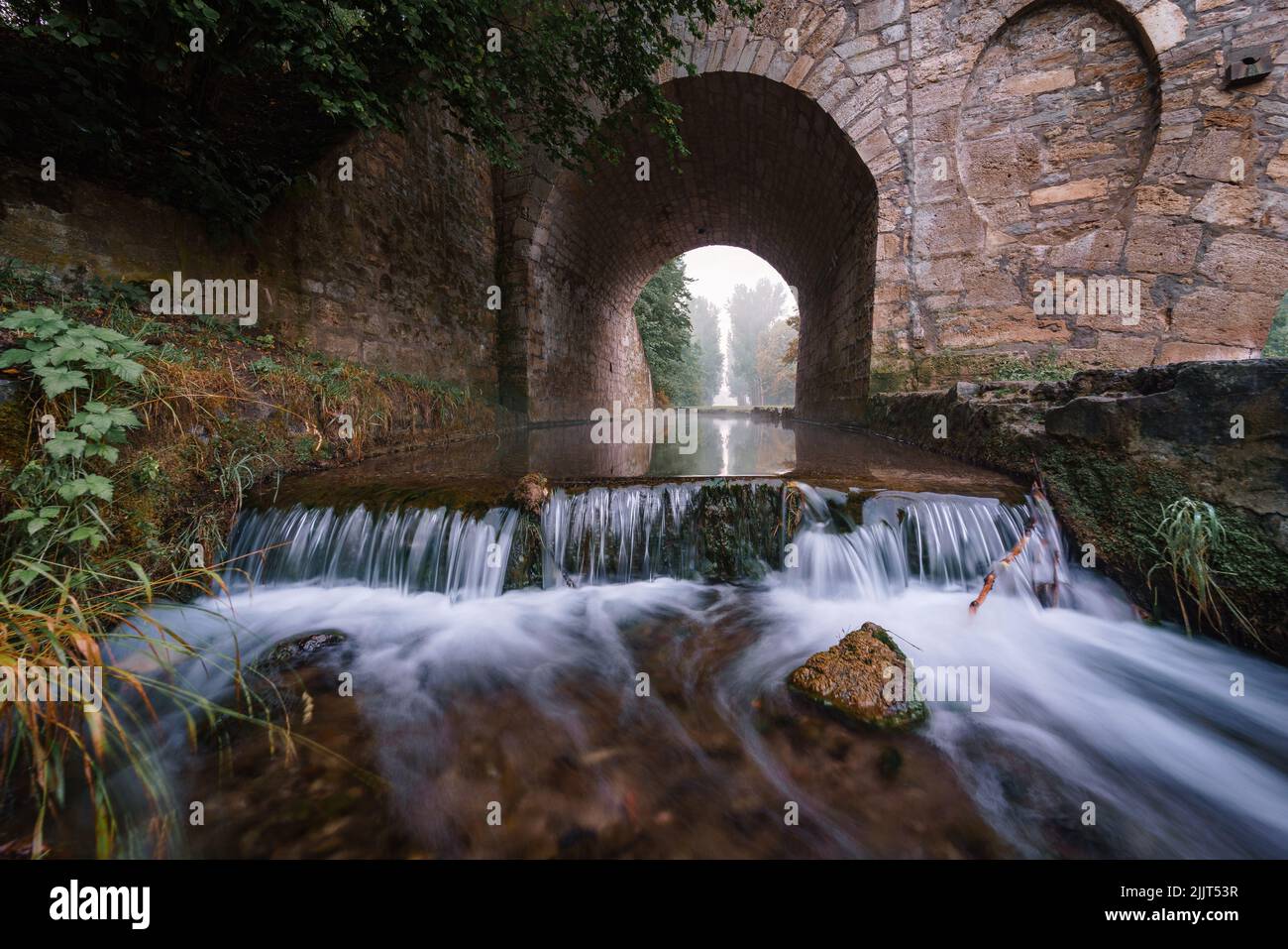 Una bella vista di Una piccola cascata che scorre sotto un ponte di pietra Foto Stock