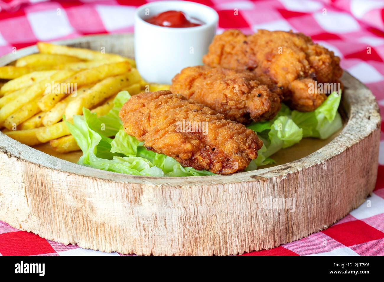Ali di pollo piccanti, con lattuga patinata e ketchup, su un piatto rustico in legno. Su una tovaglia di Gingham Foto Stock