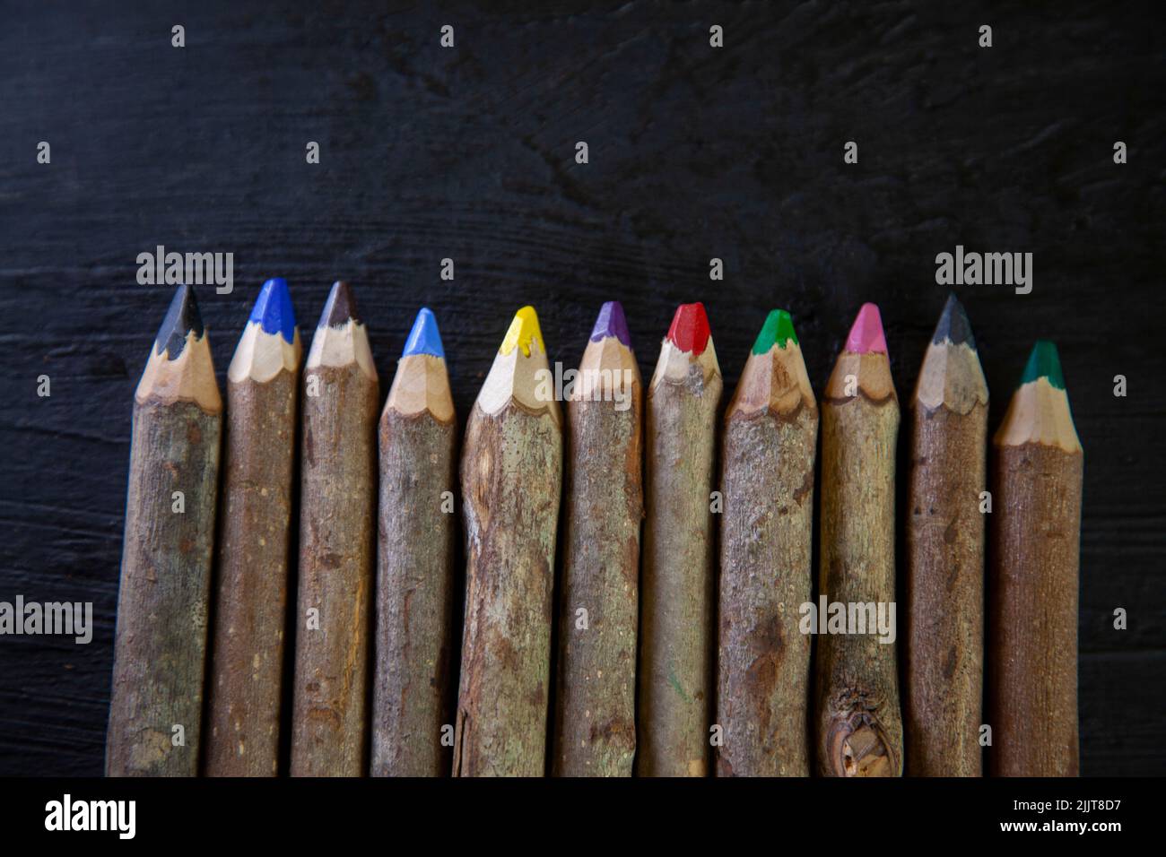 Una fila di matite di legno di colore isolate su sfondo scuro Foto Stock