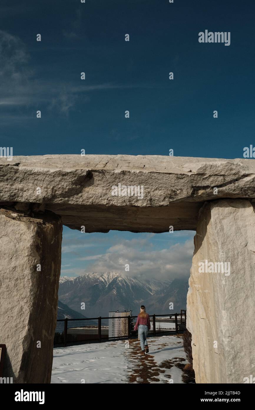 Una verticale di un monumento in pietra contro una donna caucasica che guarda le Dolomiti in Alto Adige, Italia Foto Stock