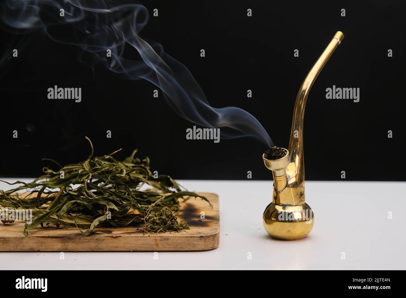 Primo piano delle foglie di cannabis su un asse di legno e fumo che esce da un tubo su sfondo nero. Legalizzazione della cannabis. Foto Stock