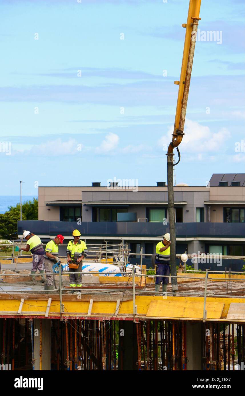 I lavoratori edili pettinano il calcestruzzo appena versato da un braccio pompato sul nuovo pavimento di un blocco di appartamenti Santander Cantabria Spagna Foto Stock