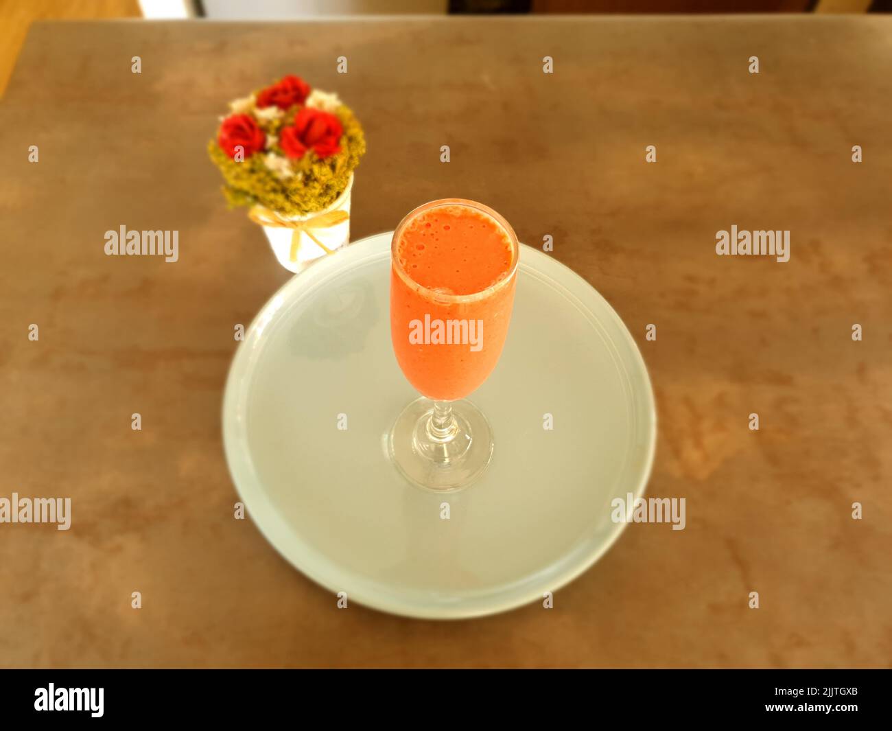 Una vista dall'alto di un bicchiere di frullato di fragola sul piatto bianco accanto ai fiori sul tavolo Foto Stock