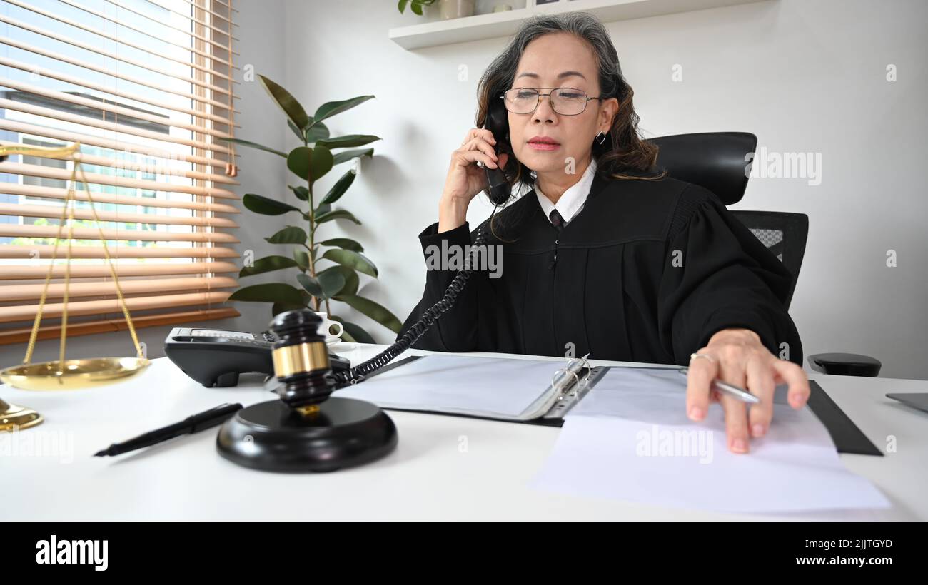 Giudice femminile maturo focalizzato o avvocato in abito uniforme lavoro con documenti contrattuali in ufficio Foto Stock