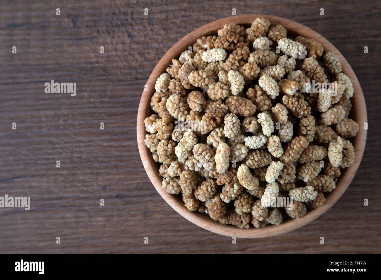 Ciotola piena di gelso secco su sfondo di legno Foto Stock