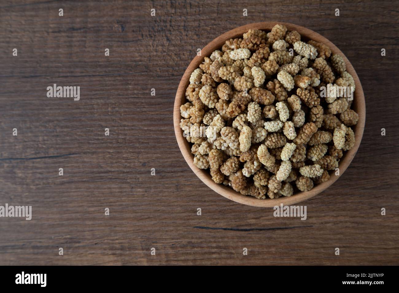 Ciotola piena di gelso secco su sfondo di legno Foto Stock