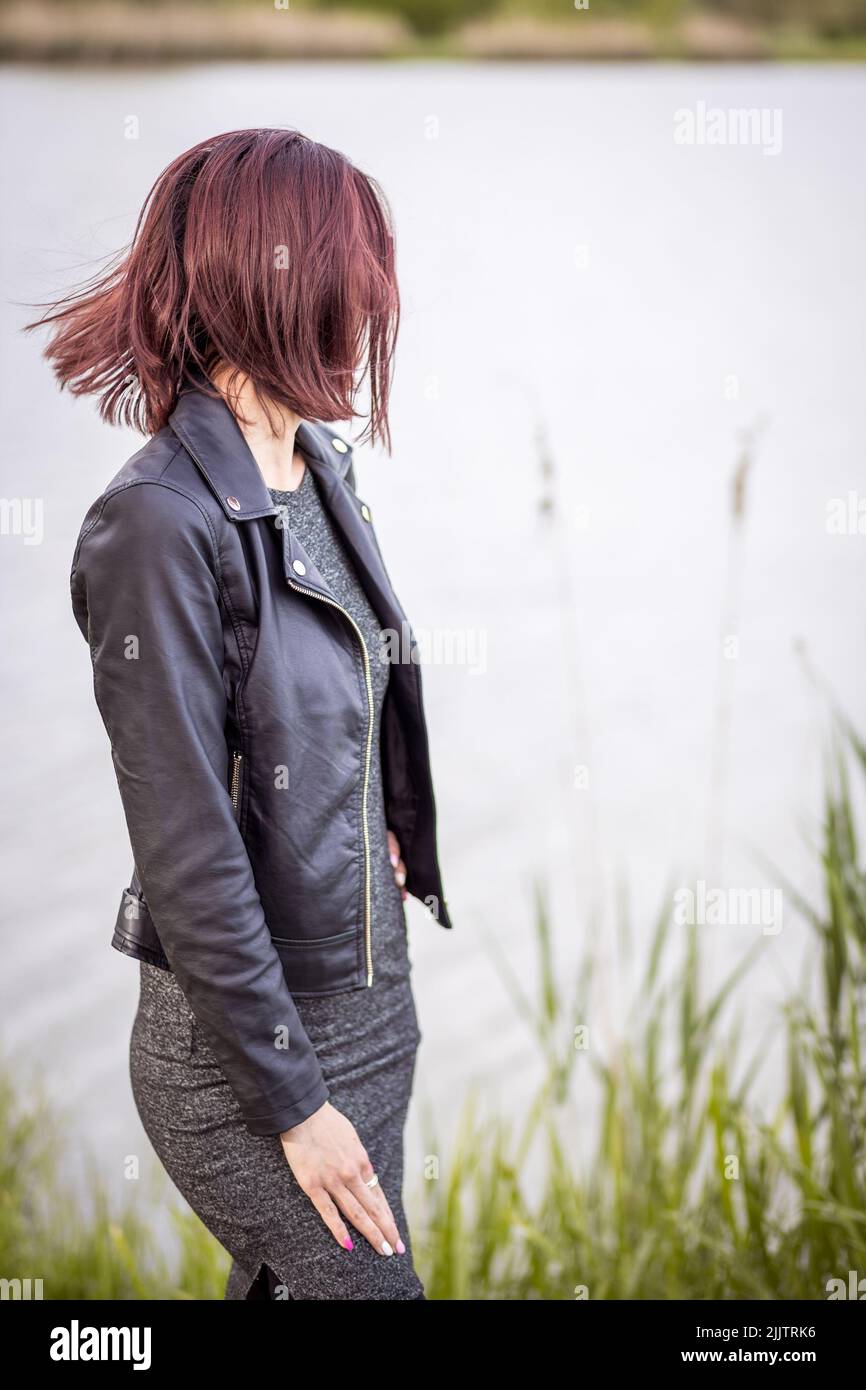 Un bel ritratto di una giovane donna che si erge accanto al lago e piante verdi nel parco in una giornata di sole Foto Stock