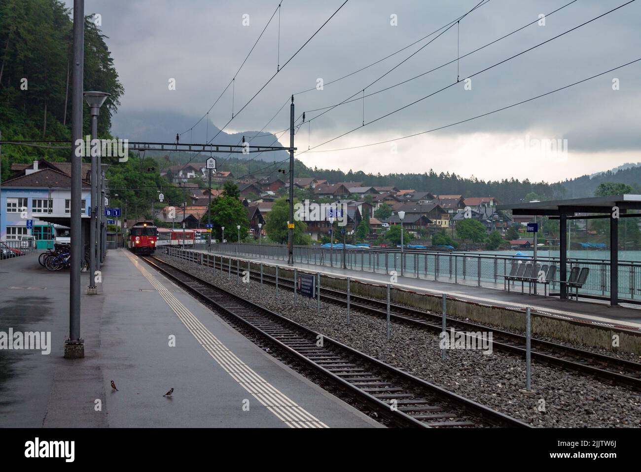 La vista sulla piattaforma esterna della stazione ferroviaria con il treno in arrivo a Interlaken, Svizzera. Foto Stock