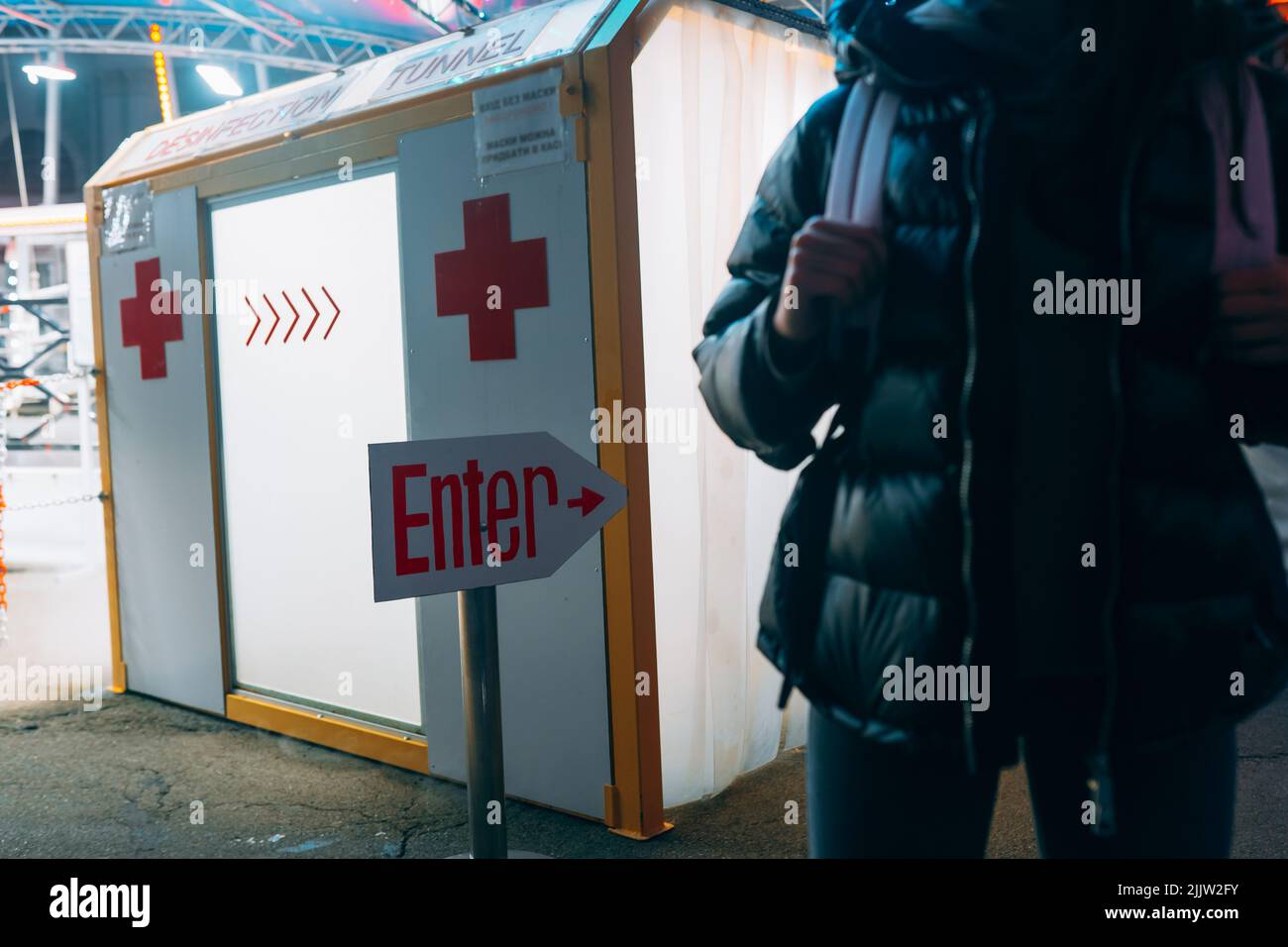 La donna in una maschera medica sta rimanendo al tunnel di disinfezione Foto Stock