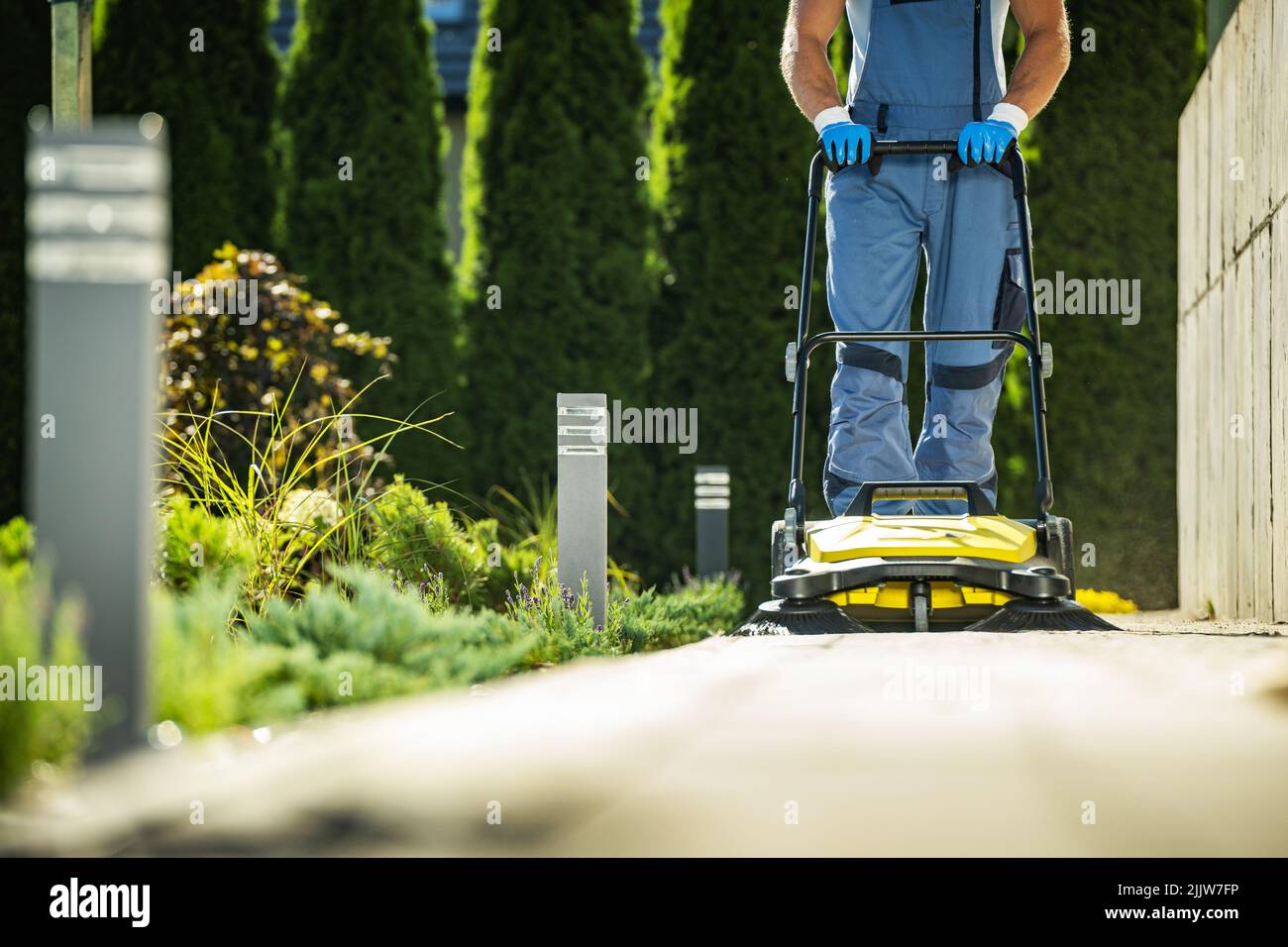 Professionista del giardiniere con percorso di pulizia del giardino della scopa a spinta. Attrezzatura di giardinaggio e paesaggistica tema. Foto Stock