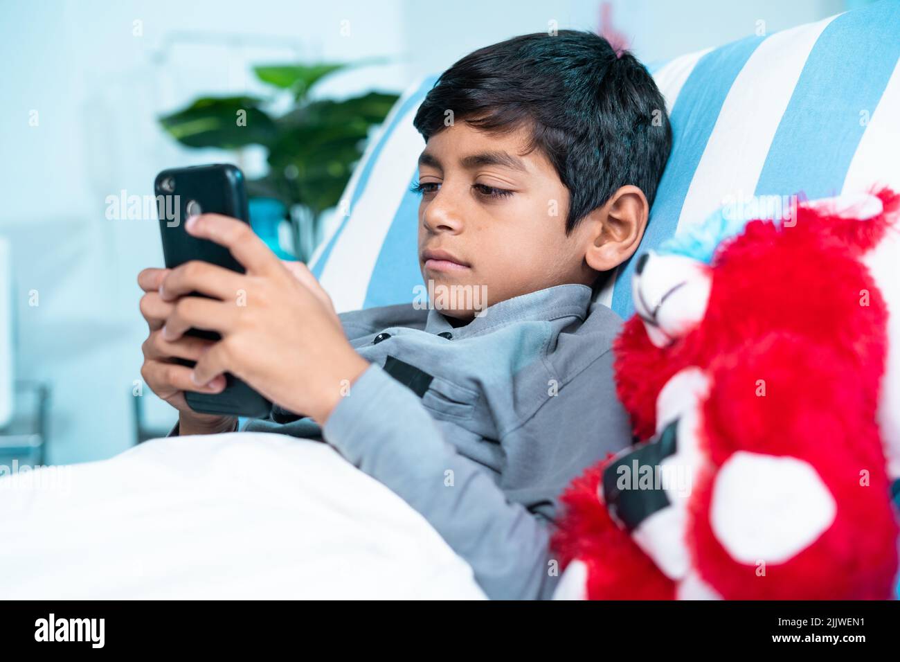 Ammessi gravi malati bambini letto utilizzando il telefono cellulare presso il reparto ospedaliero - concetto di assistenza sanitaria o medico e la tecnologia Foto Stock