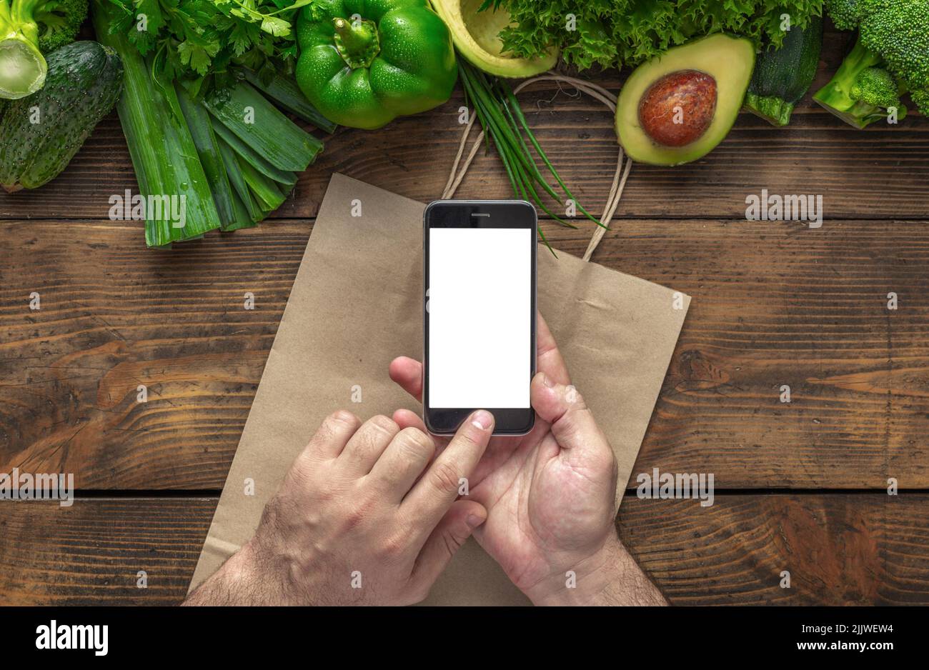 Ordinare cibo online l'uomo tiene il telefono cellulare con schermo vuoto su tavolo di legno con verdure fresche verdi vista dall'alto Foto Stock