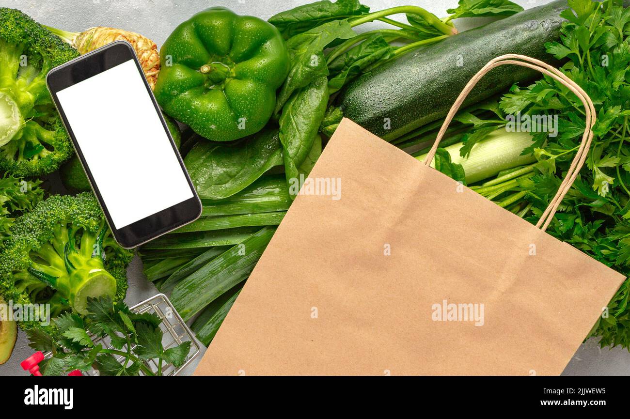 Ordina cibo online cellulare con schermo bianco sacchetto di carta e verdure verdi Acquista cibo sano Foto Stock