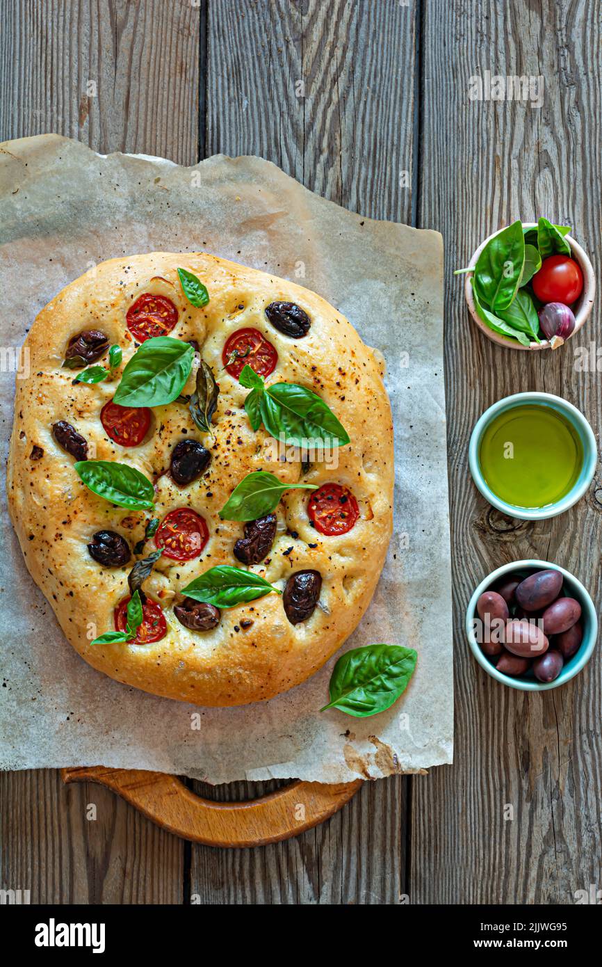 Focaccia fresca italiana con pomodori, olive, aglio ed erbe su sfondo ligneo. Foto Stock