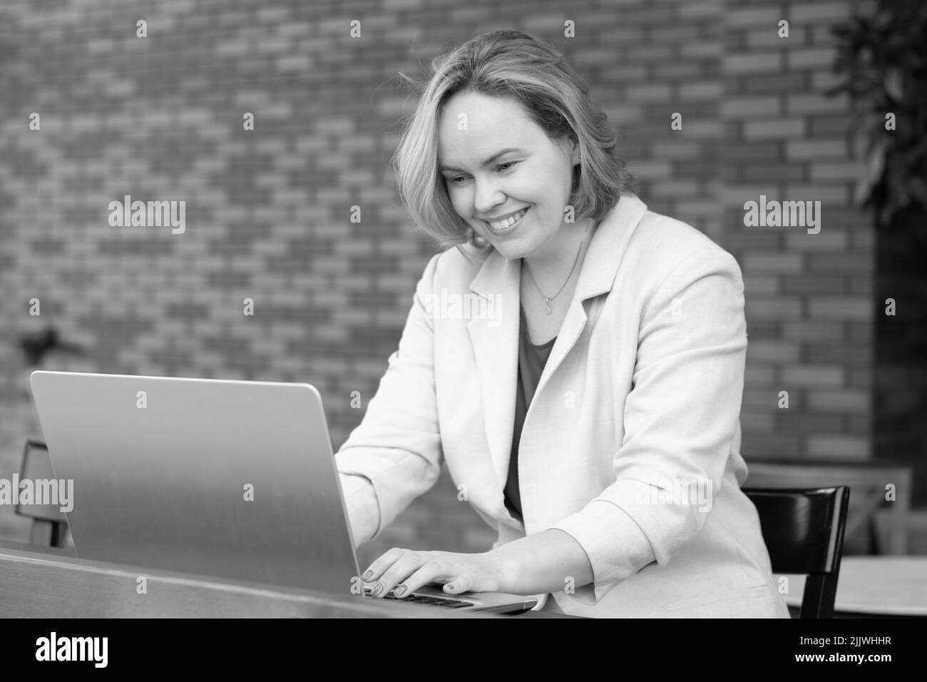 Donna sorridente felice utilizzando l'applicazione su un portatile digitale in un caffè di strada. Donna d'affari felice che lavora a distanza nel parco, usando un laptop, leggendo così Foto Stock