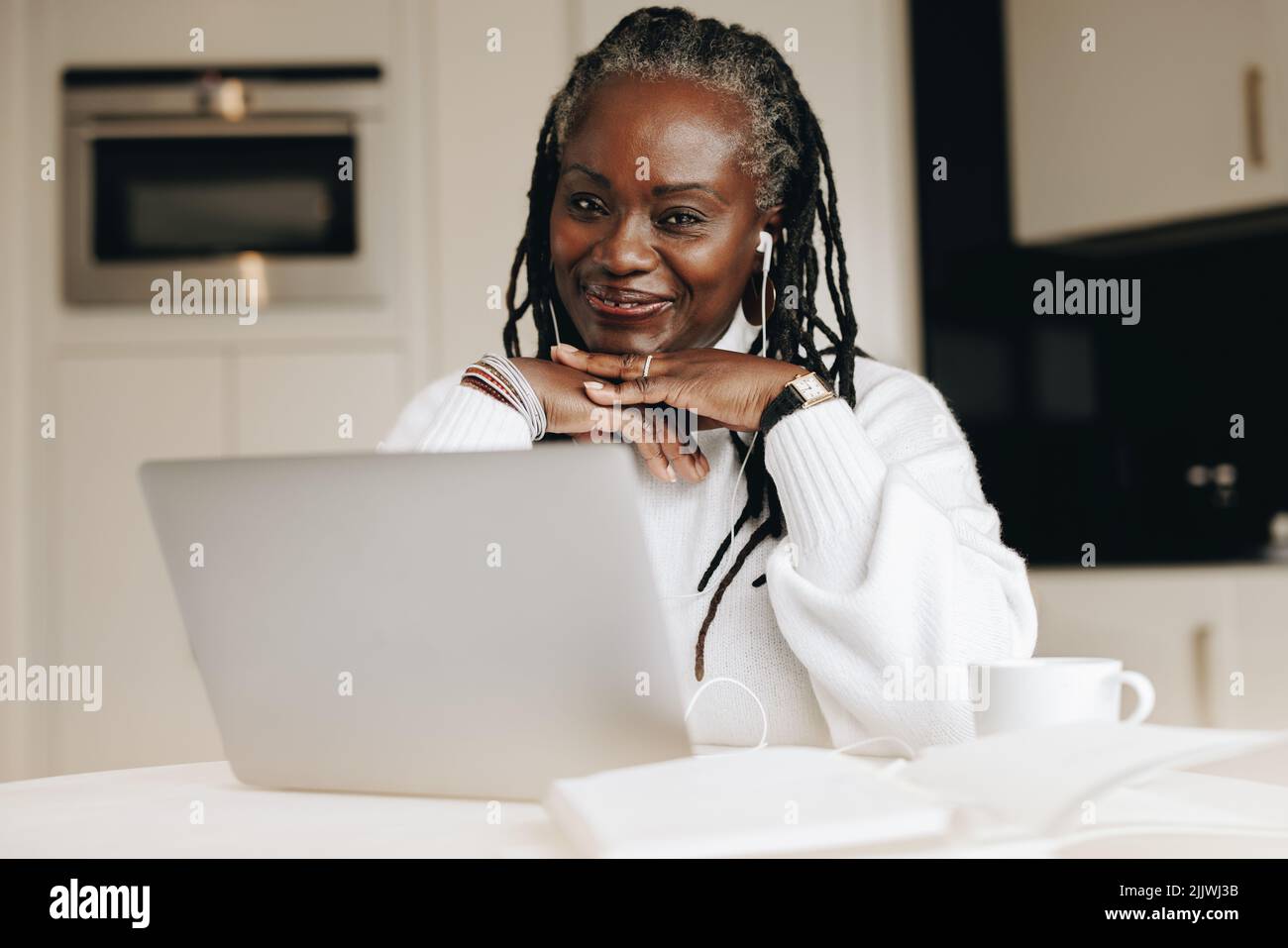 Donna d'affari allegra che guarda la fotocamera mentre lavora su un laptop nel suo ufficio domestico. Donna d'affari felice matura che ascolta la musica mentre lavora Foto Stock