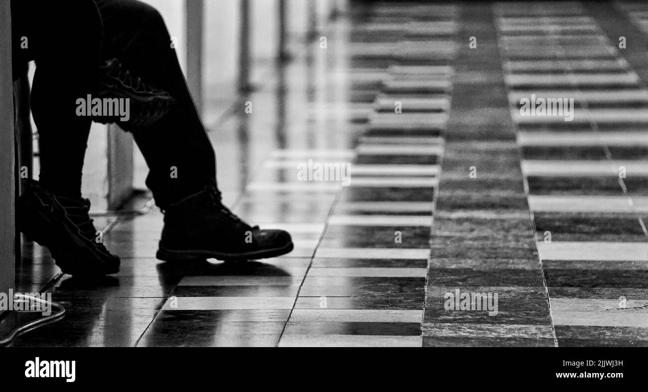 Uno scatto in scala di grigi di due paia di gambe sullo sfondo del pavimento piastrellato Foto Stock