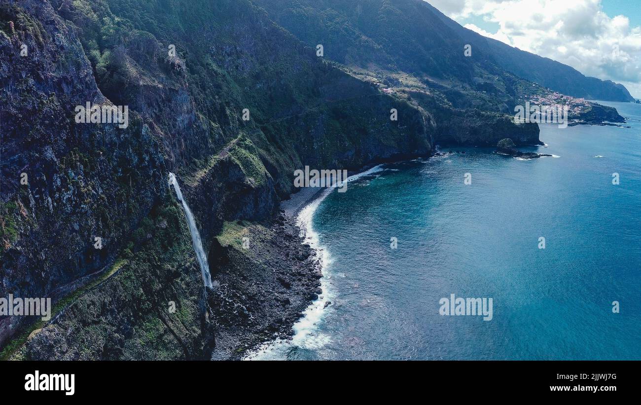 Un bellissimo paesaggio costiero con una cascata che scorre da scogliere boschive a Madeira, Portogallo Foto Stock