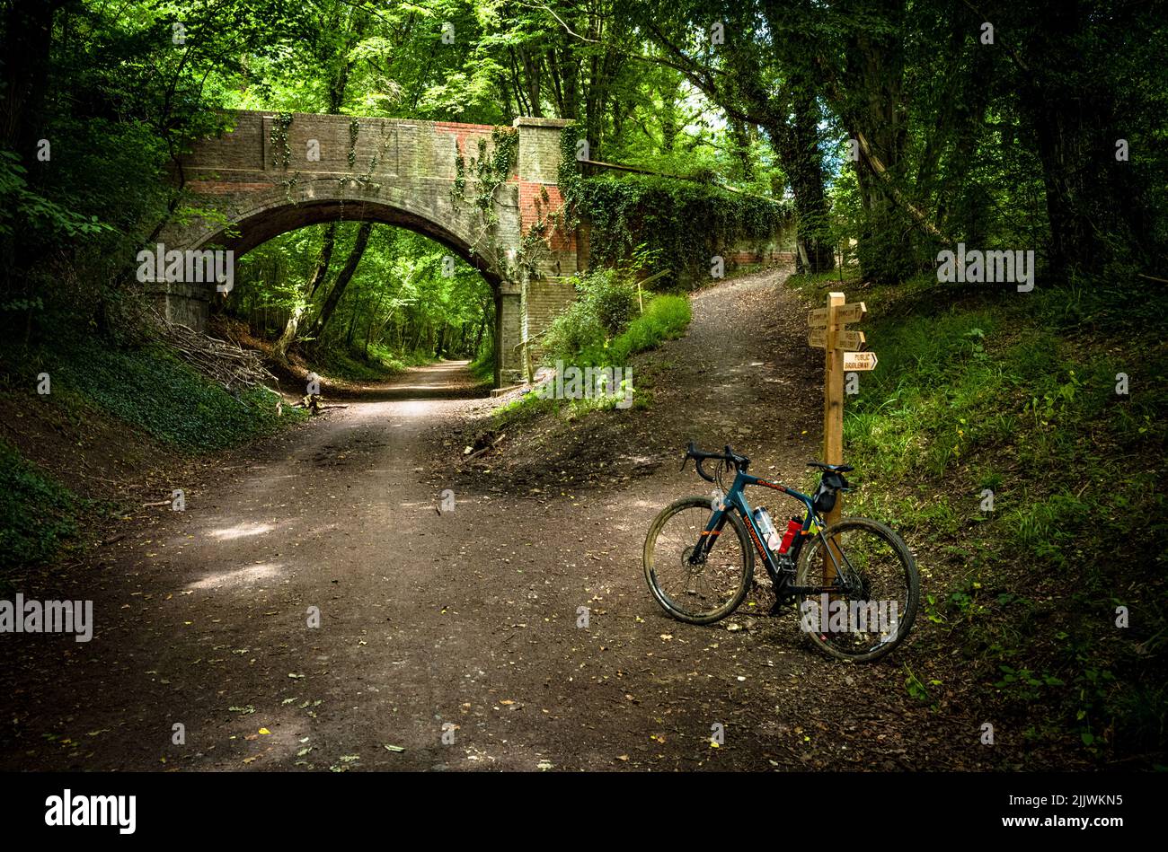 Una bici di ghiaia di Holdsworth è appoggiata contro un cartello del sentiero sul Downs link, una linea ferroviaria disutilizzata nel West Sussex, Regno Unito. Foto Stock