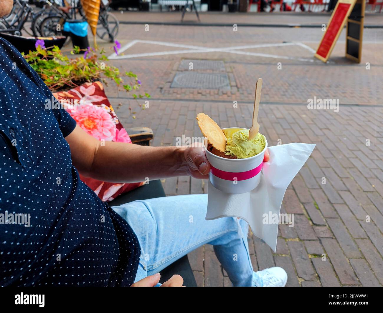 La mano bianca maschio tiene una tazza con le palette di gelato su una panca vicino ad un negozio di gelato. Non ci sono persone o marchi riconoscibili nella foto Foto Stock